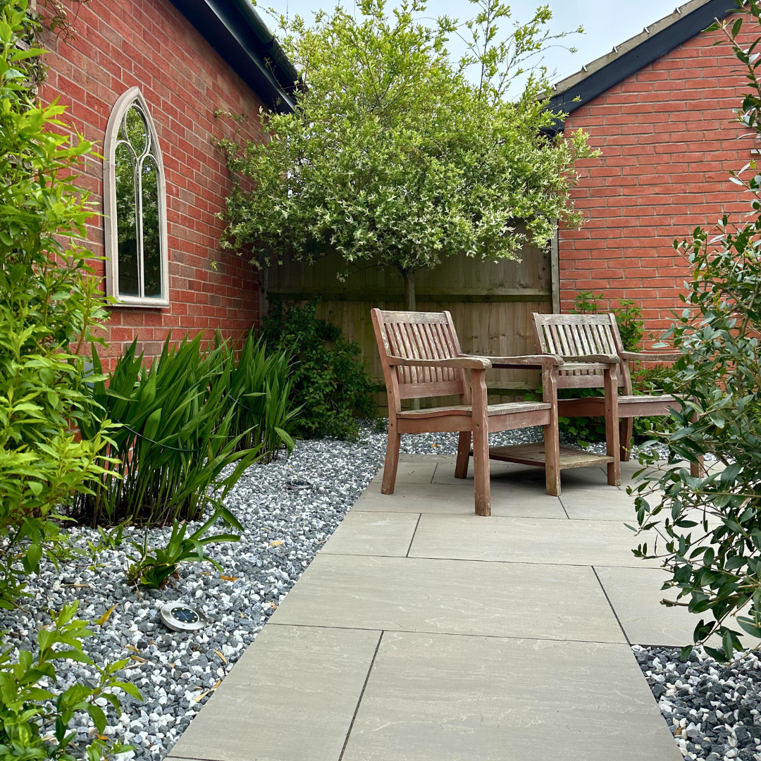 Two wooden garden chairs in the corner of a garden on Select Living Group Porcelain Paving.