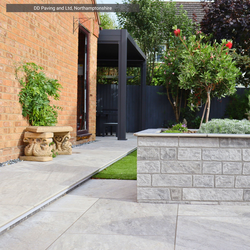 Modern garden with paved patio and  artificial grass area from Select Living Group, and a stone wall.