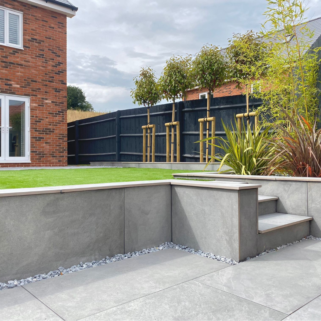 An outdoor setting featuring light grey porcelain paving from Select Living Group with a garden and house in the background.
