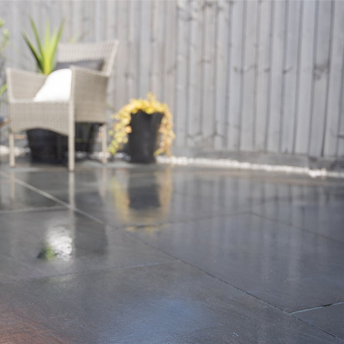 Garden photography, person reading book, sat in a garden where it has just rained, the Aravali Dark Grey porcelain paving are still wet from the rain. Installed by Up and Down Landscaping. Products provided by Select Living Group