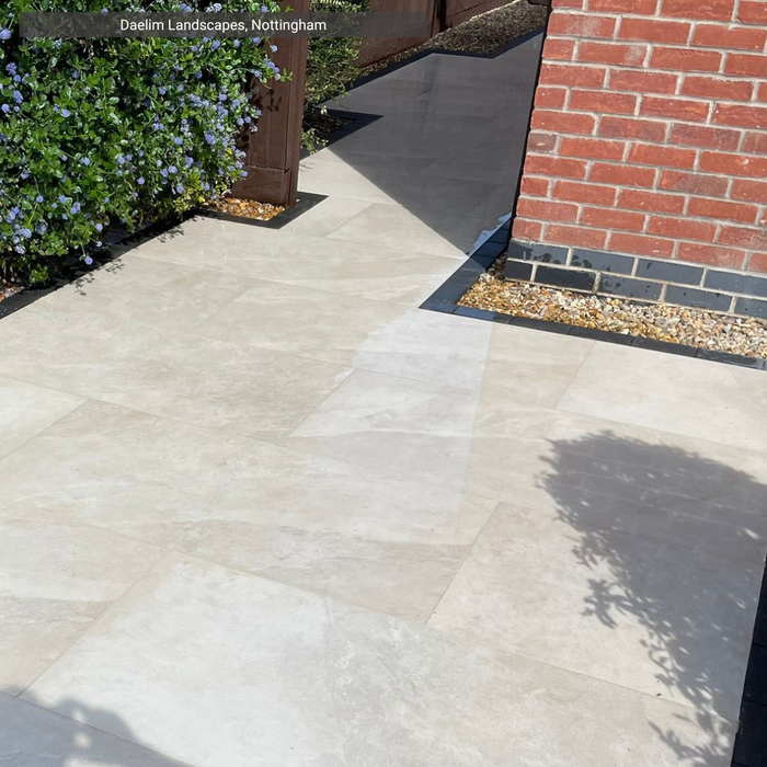 Paradiso Beige Porcelain Paving pathway from Select Living Group, with a brick wall and plants on a sunny day.