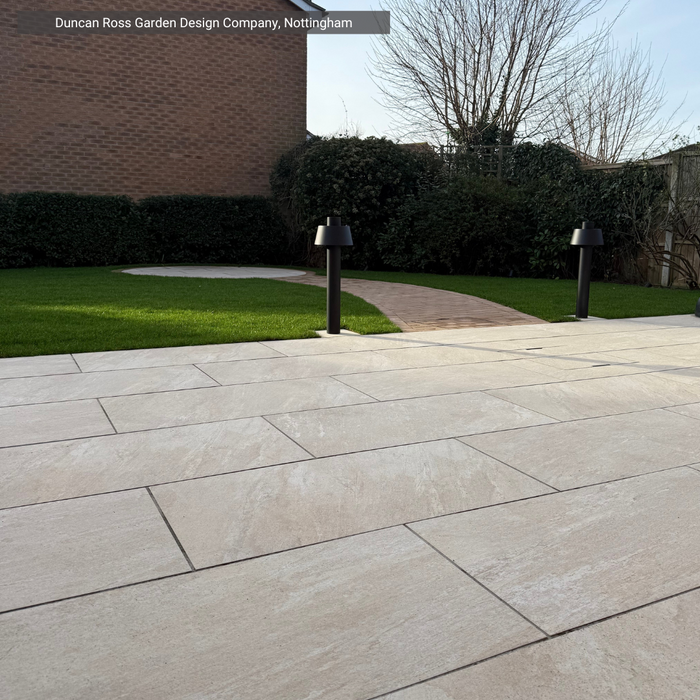 Paved patio area with grass and trees in the background, featuring Cristallo Beige Porcelain Paving from Select Living Group.
