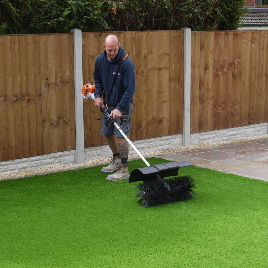 Man using a lawn edger on artificial grass with a wooden fence in the background