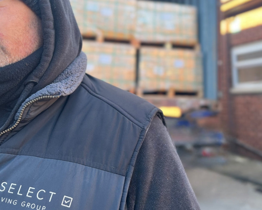 Person wearing a vest with 'SELECT LIVING GROUP' logo in an industrial setting